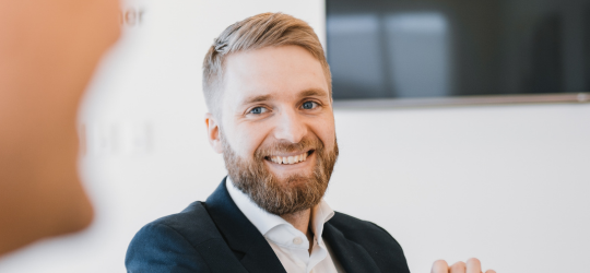 Smilende mand med skæg i mørk jakke og hvid skjorte