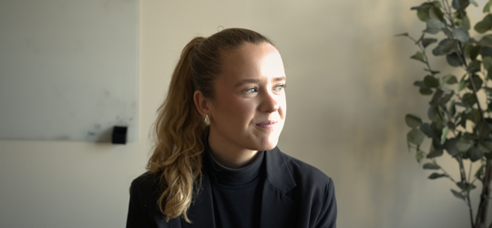 Medarbejder i mørkt tøj smiler og kigger til siden i lyst kontorlokale