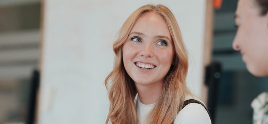 Smilende ung kvinde med langt lyst hår ser op mod en anden person