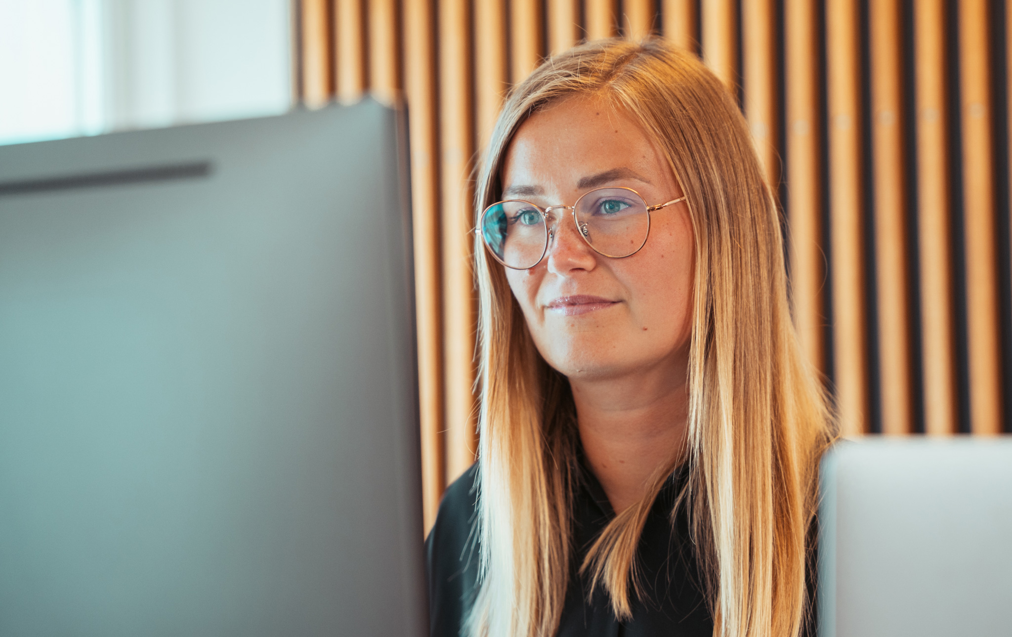 Ung kvinde med briller og langt lyst hår sidder ved computer og ser på skærmen