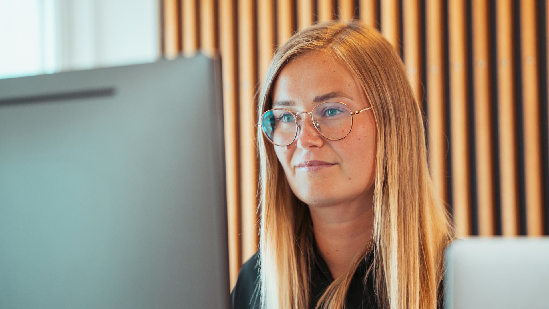 Ung kvinde med briller og langt lyst hår sidder ved computer og ser på skærmen