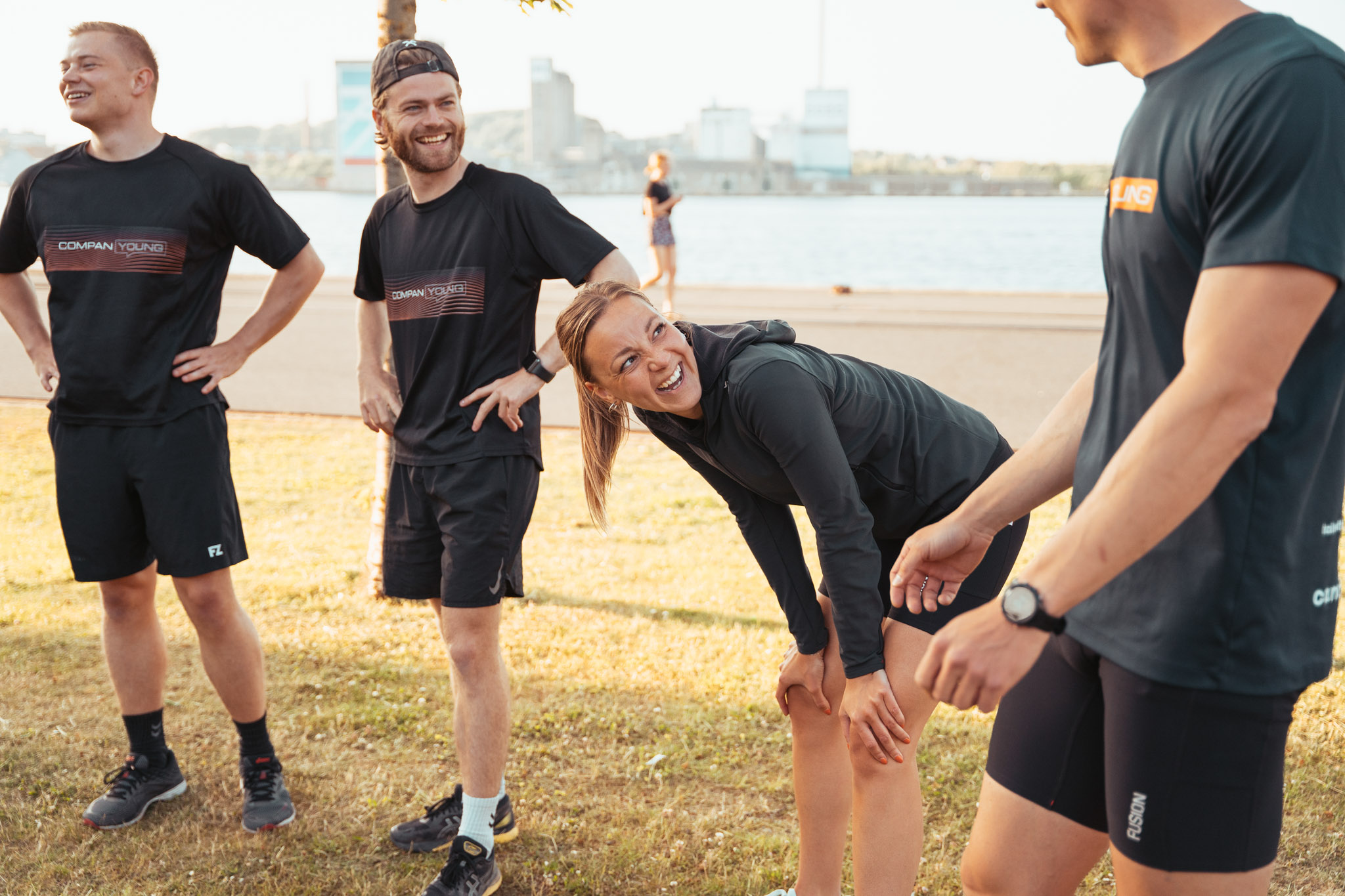 Fire unge dyrker udendørs fitness på græs ved havnefront i solskin