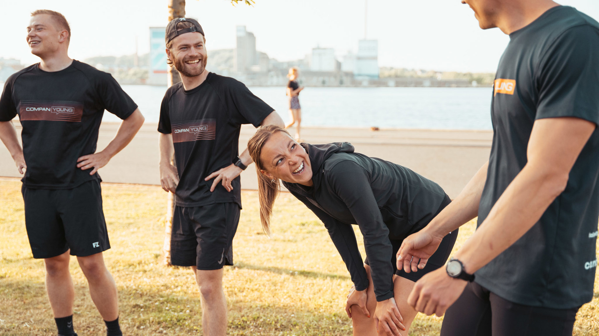 Fire unge dyrker udendørs fitness på græs ved havnefront i solskin
