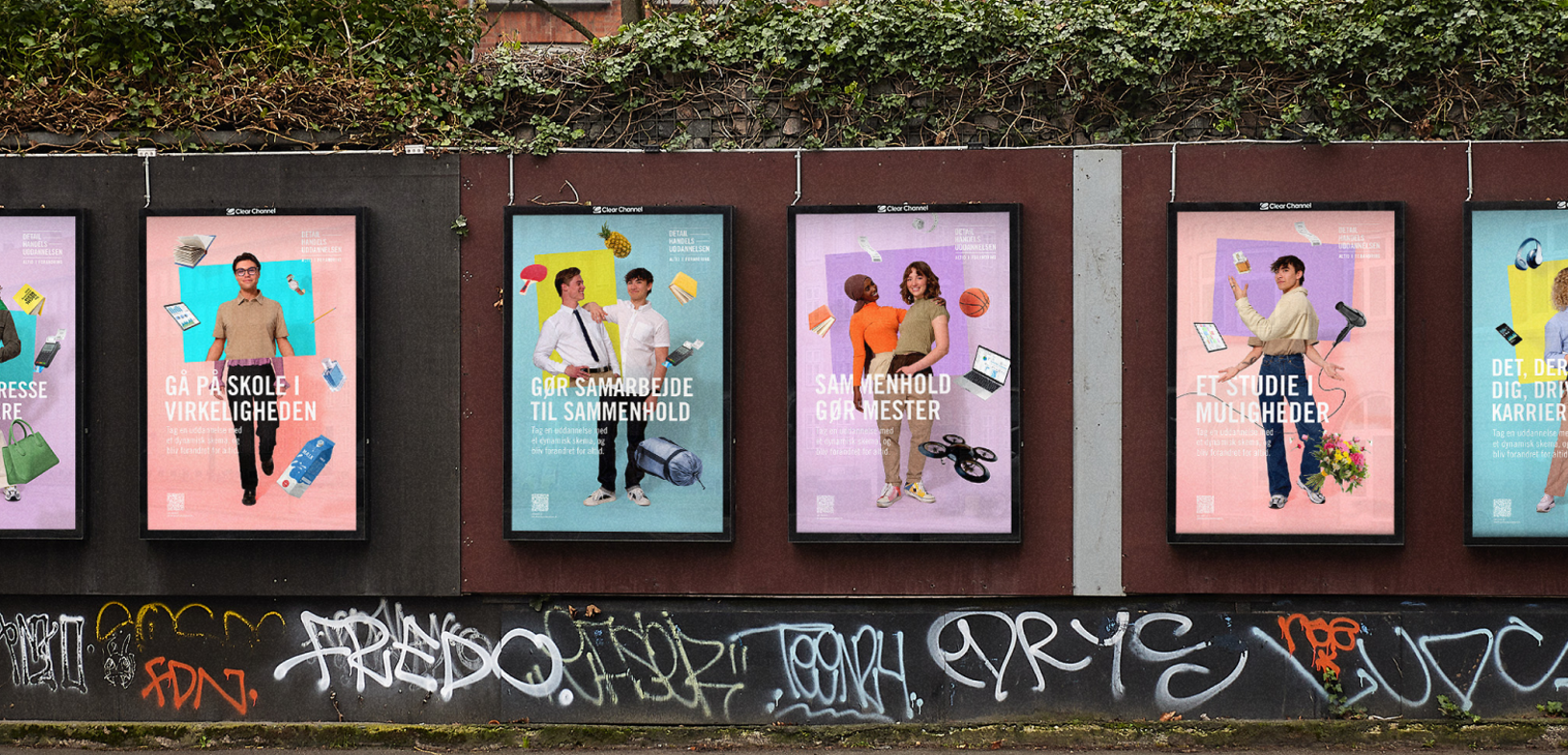 Seks farverige reklameplakater hænger side om side på en væg i byrummet med graffiti nederst og kampagnebudskaber om detailhandelsuddannelsen.