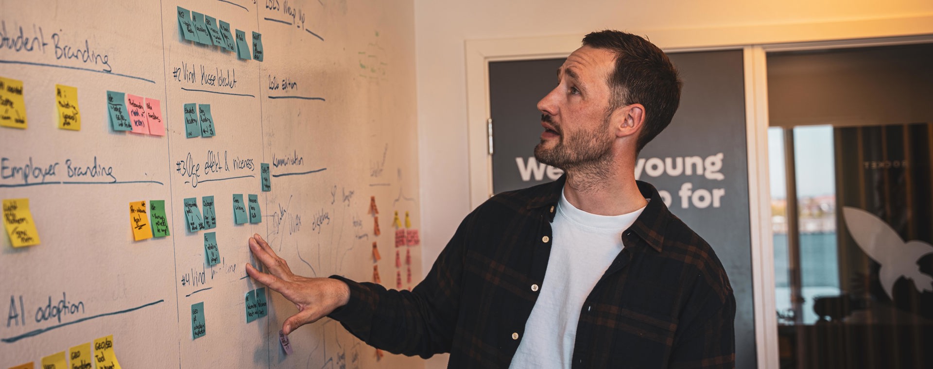 Underviser peger på whiteboard med farvede post-it notes og noter fra brainstorm
