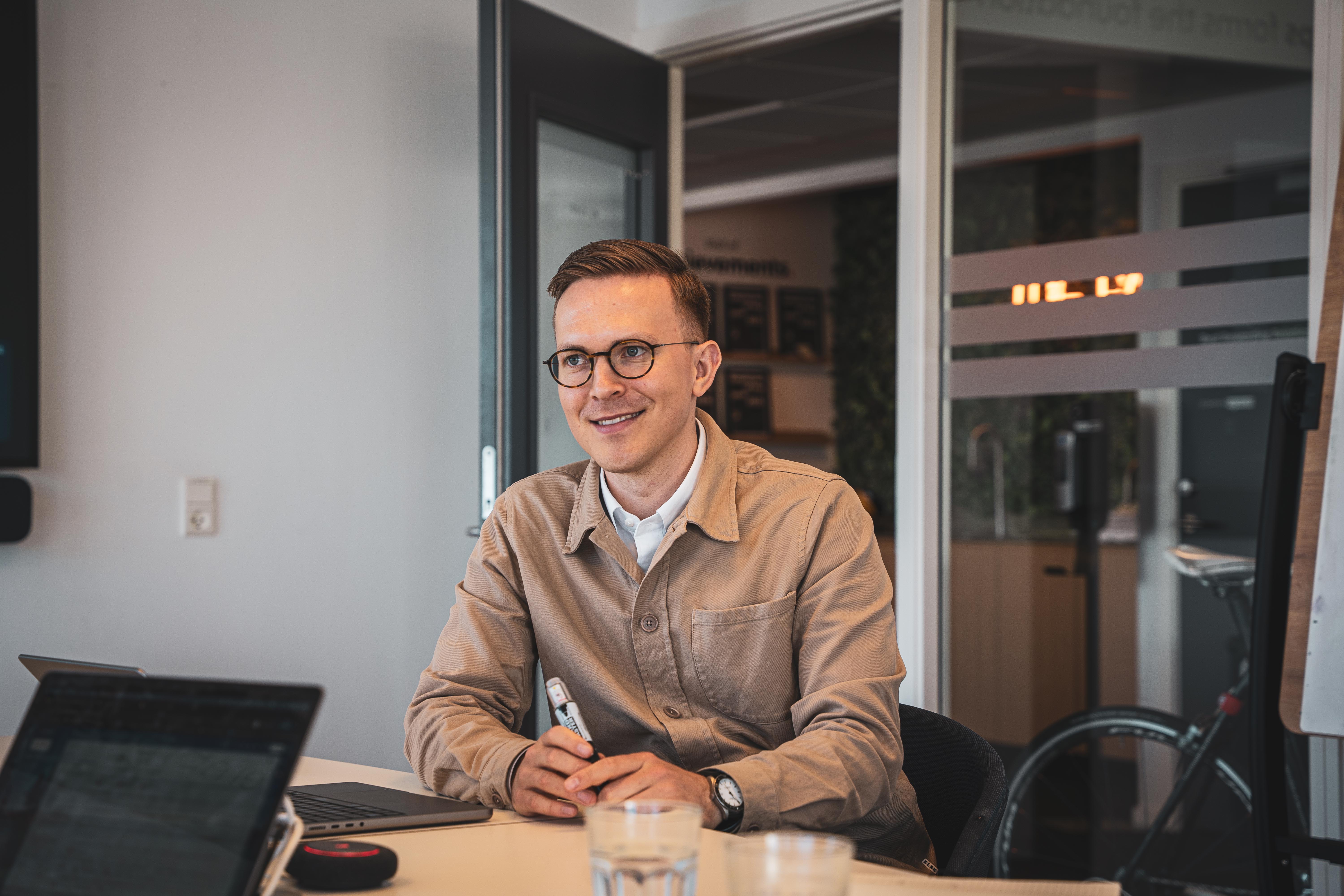Lærer eller ansat sidder ved skrivebord med computer og noterer med pen