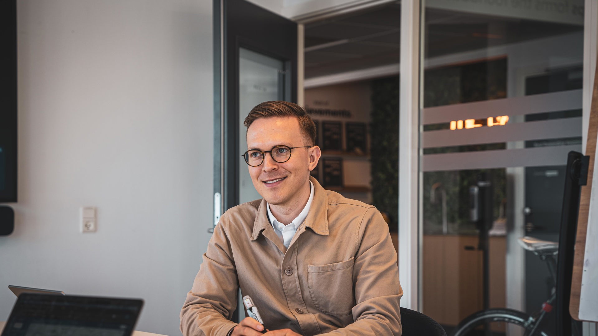 Lærer eller ansat sidder ved skrivebord med computer og noterer med pen