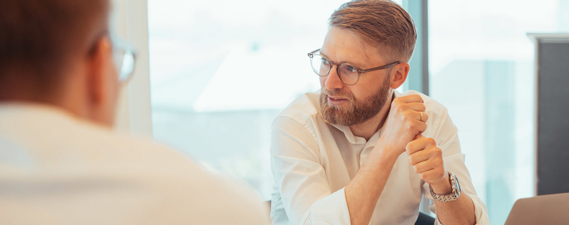 To personer i samtale ved et bord med computer og glas vand