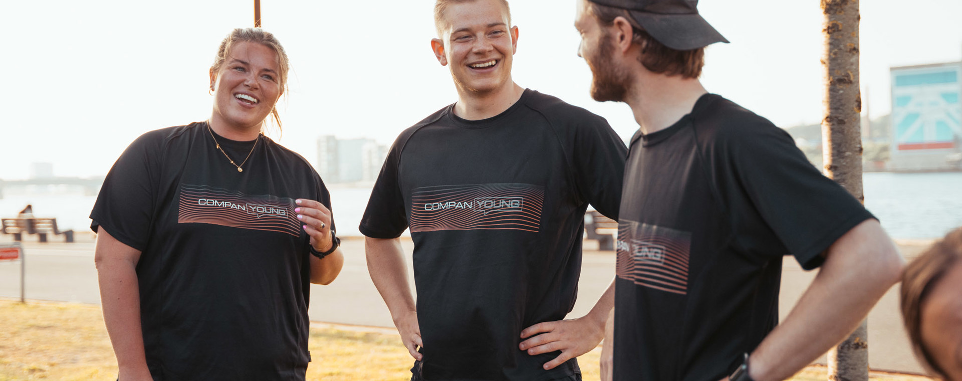 Tre unge griner sammen udendørs ved vandet i matchende sorte t-shirts