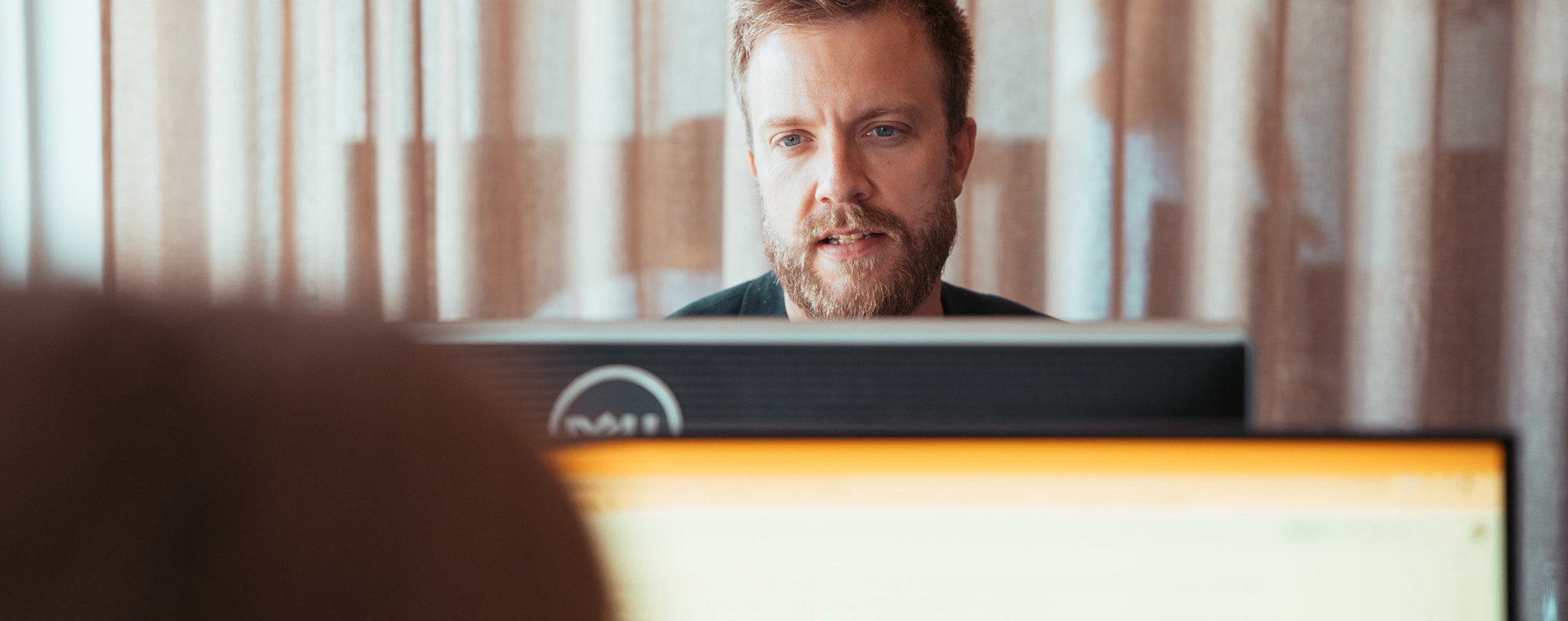 Mand med skæg sidder ved computerskærm og arbejder koncentreret