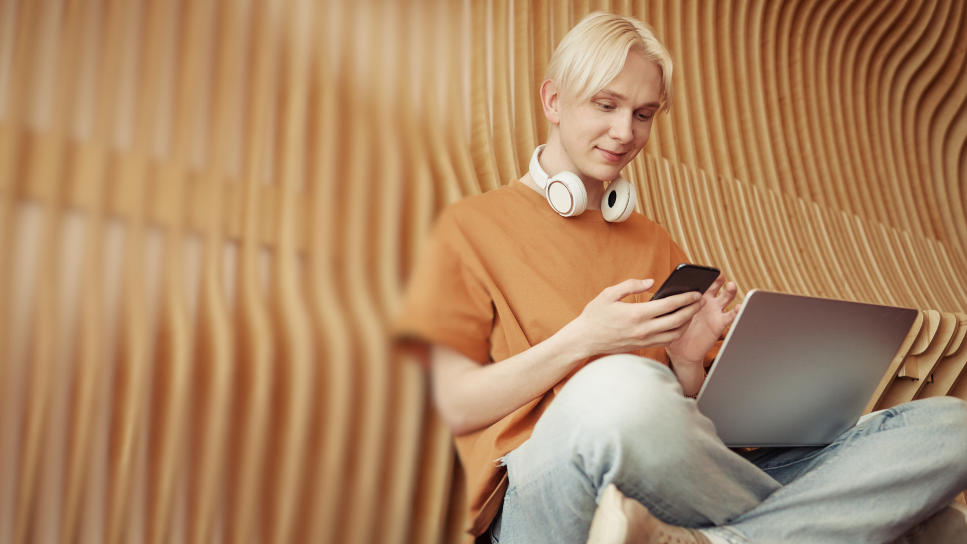 Ung person sidder med laptop og smartphone og hovedtelefoner om halsen